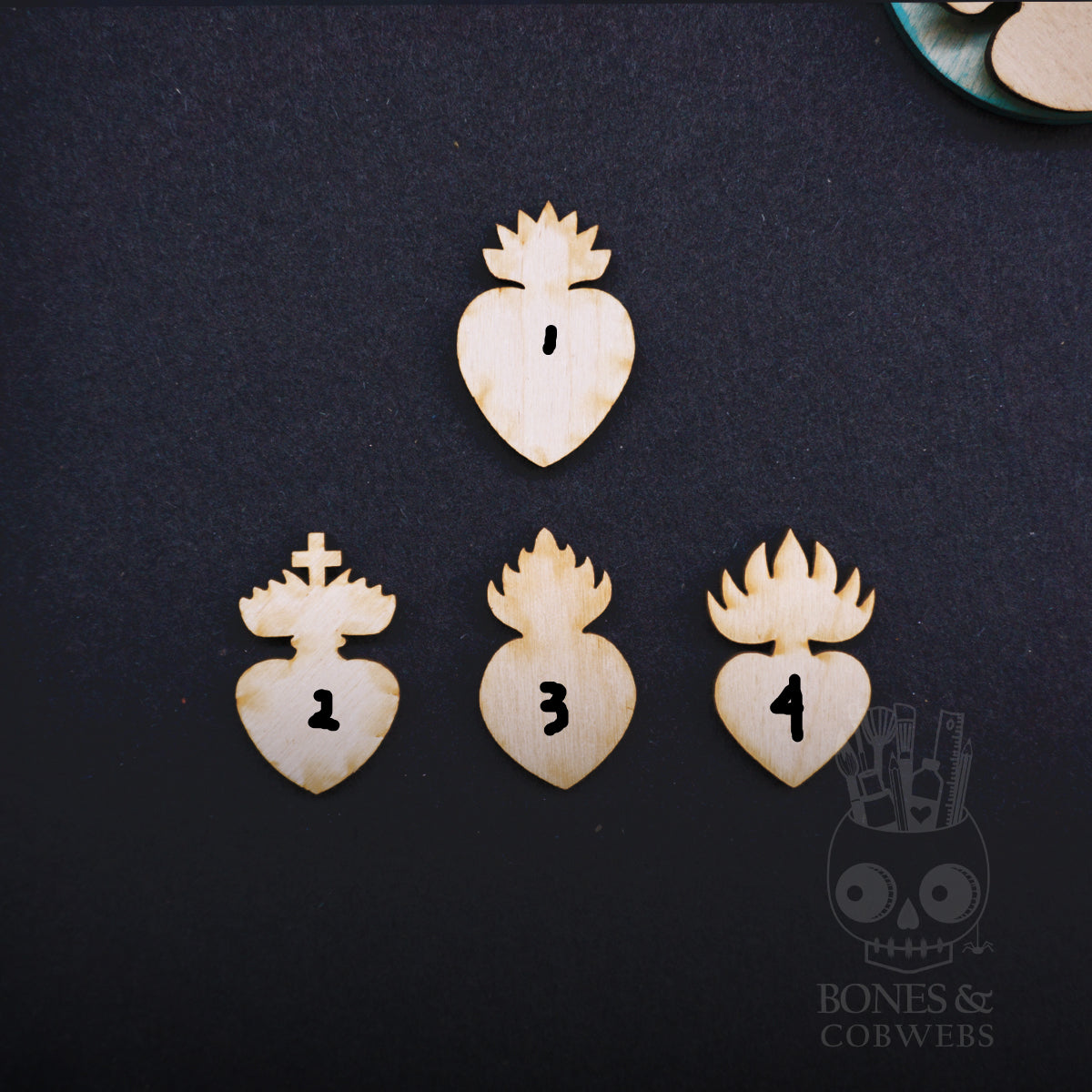 Set of four wooden heart-shaped charms on a dark background, branded 'Bones & Cobwebs'.