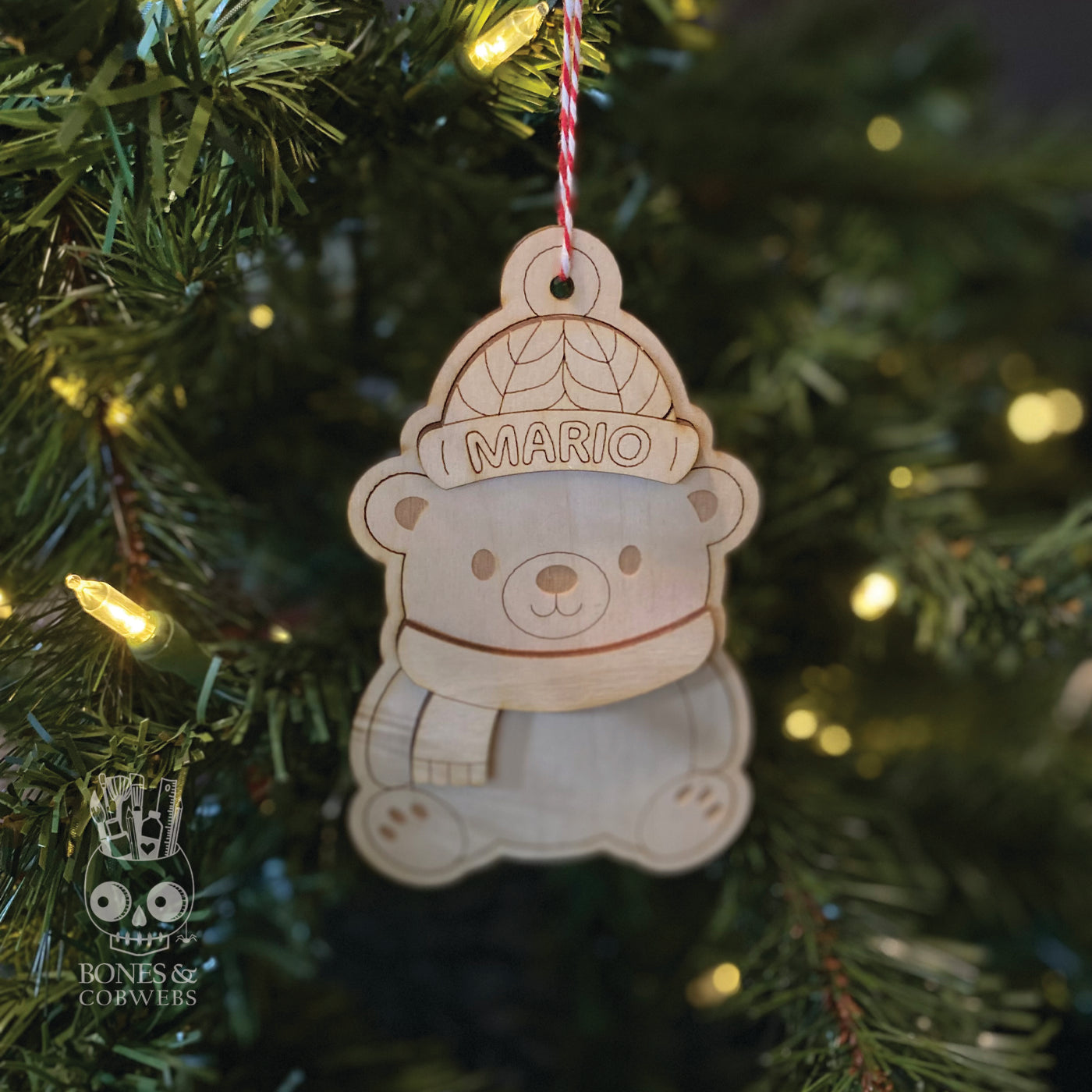 Personalized wooden ornament shaped like a bear with 'MARIO' text, hanging on a Christmas tree. 