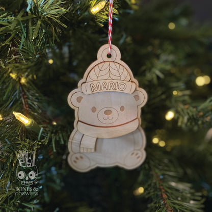 Personalized wooden ornament shaped like a bear with 'MARIO' text, hanging on a Christmas tree. 
