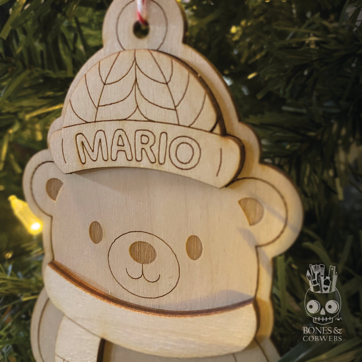 Close up of wooden bear ornament with 'MARIO' beani hanging on a Christmas tree.